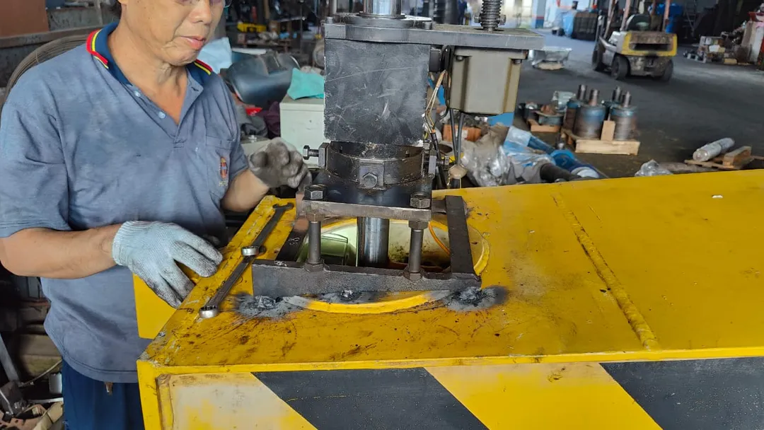 Technician operating a drill press on a steel frame component